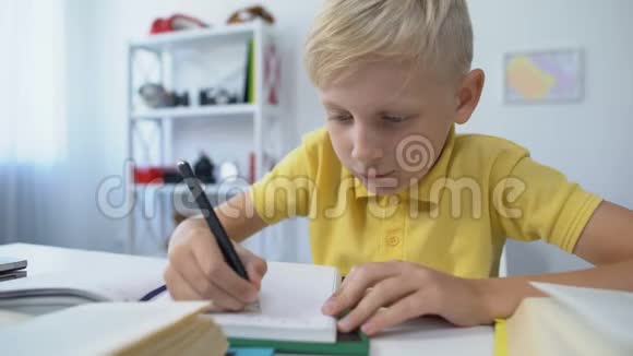 金发男孩子在笔记本上写面具把头放在桌子上无聊视频的预览图
