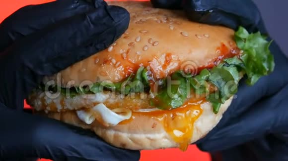 近距离观看一个大多汁的汉堡包里面有一个鸡蛋一个番茄切割机沙拉和红酱双手戴黑色手套视频的预览图