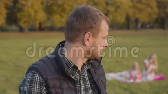 微笑的白种人男子向他的女儿们挥手在背景和看相机父亲在家野餐视频的预览图