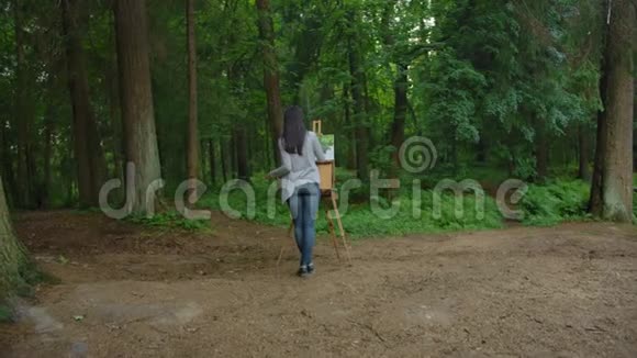 女孩画风景站在公园的画架前视频的预览图