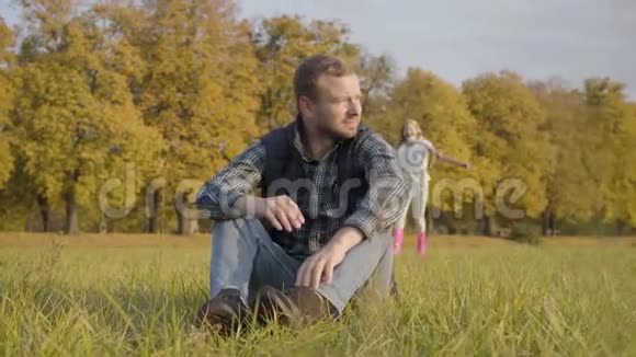 微笑的白种人女孩穿着休闲服和粉红色的橡胶靴跑到一个男人坐在秋天的草地上金发美女视频的预览图