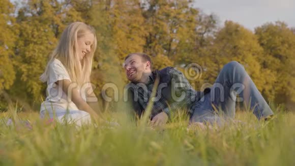 父女俩坐在秋天的草地上聊天穿着休闲服装的白人男子和年轻金发女孩视频的预览图