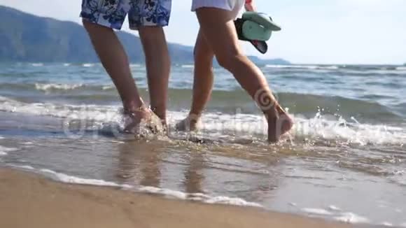 年轻夫妇的腿在海洋背景下沿着海滩一起行走在海边散步和泼水视频的预览图