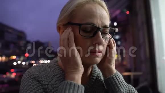 疲惫的成熟女人按摩太阳穴感到头痛大城市的喧嚣视频的预览图