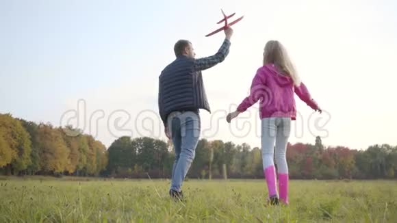 后景白种人男子和年轻的金发女孩漫步和旋转在秋天的草地上爸爸拿着粉红色的玩具视频的预览图