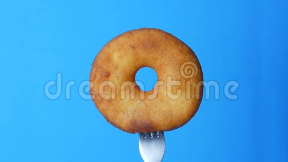 叉子上的圆形大甜甜圈上面有巧克力糖霜和蓝色粉末在蓝色的背景上旋转视频的预览图