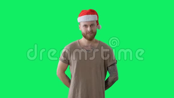 身穿绿色t恤戴着红色圣诞帽长着胡须的年轻纹身男正在用彩色钥匙给相机送礼物视频的预览图