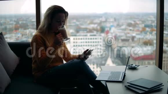 一个女人坐在城市风景旁边拿着咖啡和电话视频的预览图