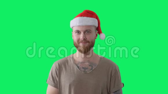 年轻英俊的留着胡须的纹身男穿着绿色t恤戴着红色圣诞帽背景是彩色钥匙孤立的肖像视频的预览图