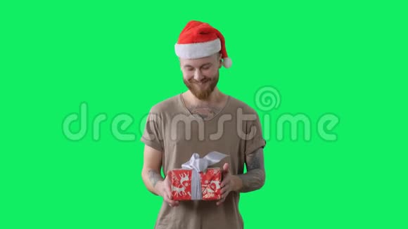 身穿绿色t恤戴着红色圣诞帽长着胡须的年轻纹身男正在用彩色钥匙给相机送礼物视频的预览图