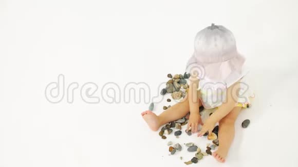 戴桶帽的小女孩在白色背景上玩海鹅卵石和贝壳假期相关剪辑视频的预览图