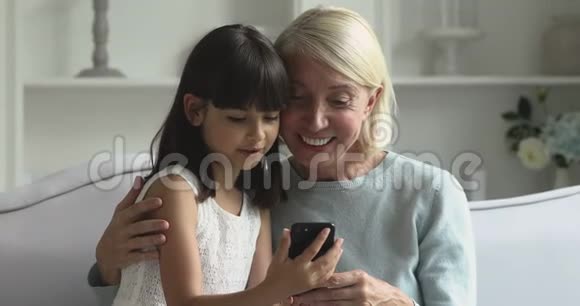 快乐成熟的奶奶和孙女在家里用智能手机视频的预览图