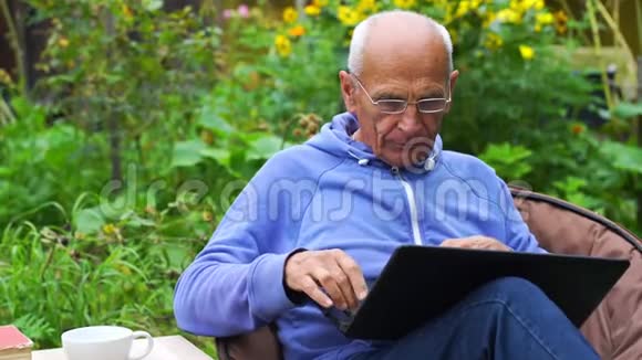 戴眼镜的严肃老人在后院的笔记本上工作视频的预览图