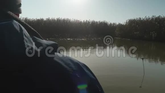 从站在河上的船上看到芦苇和河面准备钓鱼背光的芦苇男人休闲视频的预览图