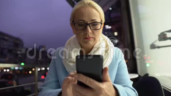 严肃的女性在晚间露台或阳台上看智能手机上的电子邮件视频的预览图