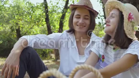 可爱的白种人夫妇坐在公园里微笑着说话留着长发的男人和戴帽子的漂亮女人视频的预览图