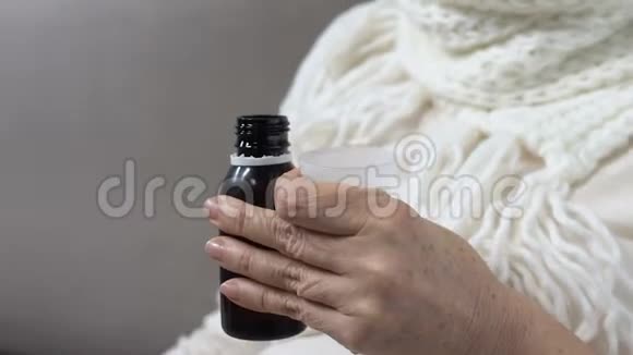 戴围巾的成熟女人服用恶心的止咳糖浆治疗流感的药物视频的预览图