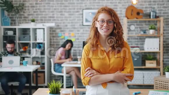 戴着眼镜的红发女人站在办公室双臂交叉微笑视频的预览图