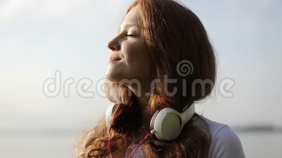 慢动作跳舞的年轻快乐女人的肖像红色卷发脖子上戴着耳机视频的预览图