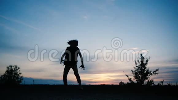 一个留着长发的男孩在日落时跳嘻哈舞的剪影视频的预览图