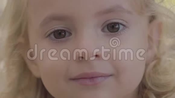 一个金发棕色眼睛的小漂亮女孩的特写肖像看着相机微笑着可爱视频的预览图