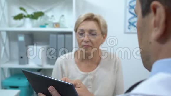 治疗师在平板电脑上显示快乐老年女性病人的健康检查结果视频的预览图