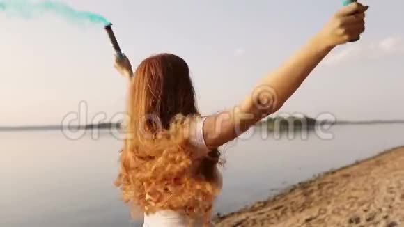 一个长着雀斑的红发女孩带着蓝色的五颜六色的烟雾在河岸上奔跑视频的预览图