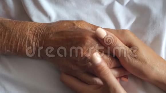 女人抱着温柔抚摸着生病母亲的手给予支持女儿安慰她年迈的皱纹手臂视频的预览图
