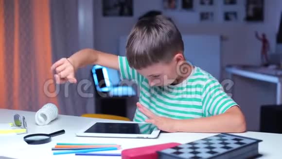 一个男孩坐在桌子旁上学时用平板电脑视频的预览图