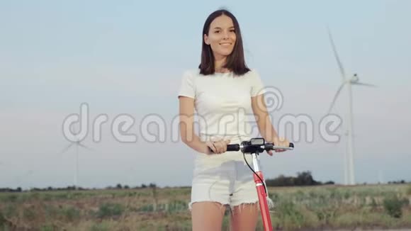 一个女孩带着她的电动滑板车在风力发电站的背景下在晚上视频的预览图