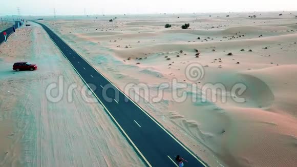 女孩骑着滑板在沙丘之间的沙漠道路上Drun射击视频的预览图