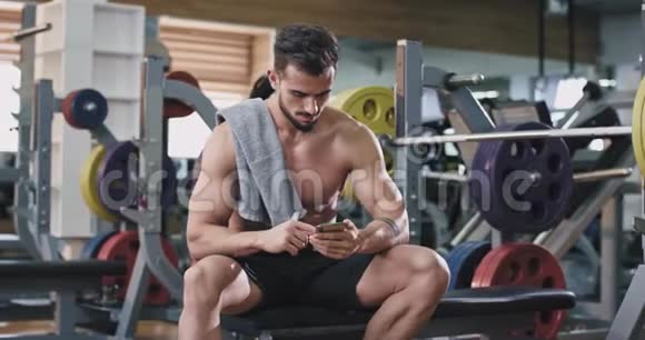 一个英俊的年轻人在健身房时看着他的手机开始喝水视频的预览图