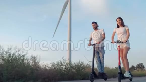 一个男人和一个女孩骑电动滑板车旁边的巨大风力涡轮机视频的预览图