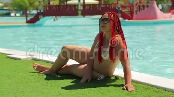 游泳池边的一位年轻的黑发女人穿着泳衣打日光浴视频的预览图