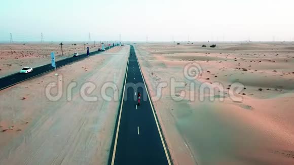 女孩骑着滑板在沙丘之间的沙漠道路上Drun射击视频的预览图
