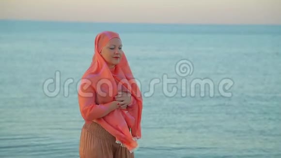 一个穿着橙色披肩的年轻穆斯林女人在海滨散步视频的预览图