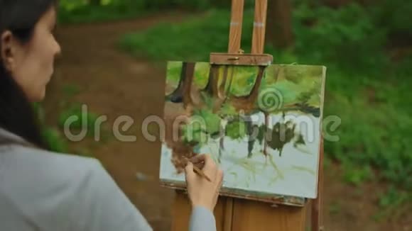 一个年轻的黑发女孩在森林里画了一幅画油画布上的风景视频的预览图