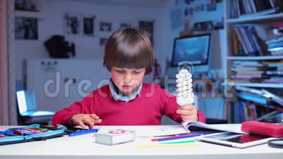 男孩坐在桌子旁手里拿着灯泡摇着它视频的预览图