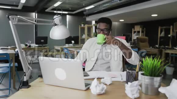 年轻的非洲男人正在电脑上工作在办公室里喝咖啡或茶视频的预览图