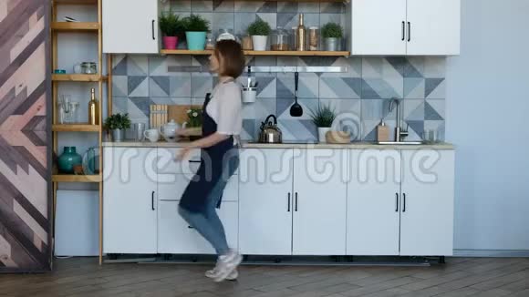 漂亮的年轻女人在厨房里跳舞听音乐视频的预览图