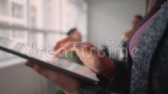 在办公室里一位女企业家用数码平板电脑站在同事面前进行谈话视频的预览图