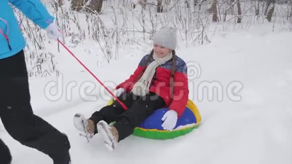 快乐的母亲骑着一个孩子在白色的雪道上雪橇上圣诞节假期成人和儿童的有趣游戏这就是视频的预览图