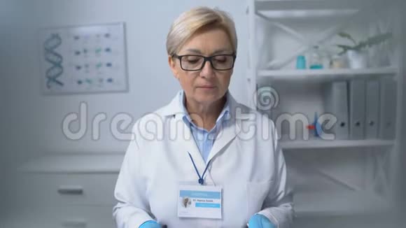 戴眼镜的善良的女医生坐在桌子旁对着摄像机工作人员微笑视频的预览图