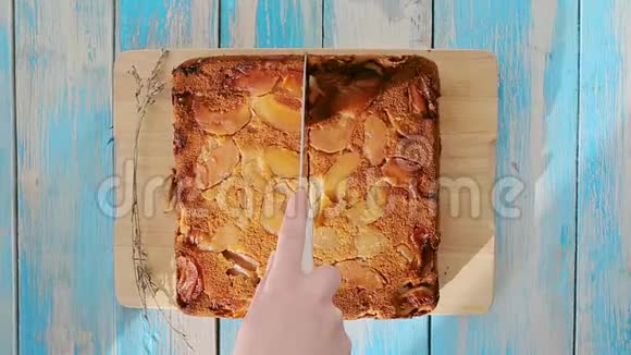 女人的手把苹果派切成两半平躺着快关门蓝色木制背景自制食品的概念视频的预览图