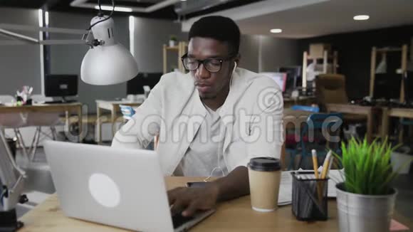 非洲商人使用笔记本电脑在现代办公室看文件视频的预览图