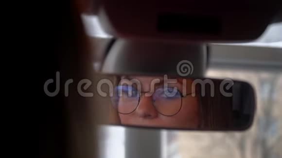 戴眼镜的漂亮女人在车里的后视镜里看着视频的预览图