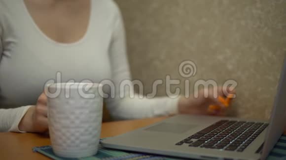 年轻女子在厨房的笔记本电脑上工作在笔记本电脑上打字模拟喝茶视频的预览图