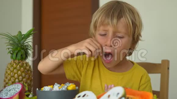 一个穿黄色衬衫的小男孩吃一种激情水果或马拉库贾它很酸很多热带水果都在视频的预览图