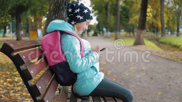 金秋时节一位美丽的少女坐在公园的长凳上用手机网上概念视频的预览图