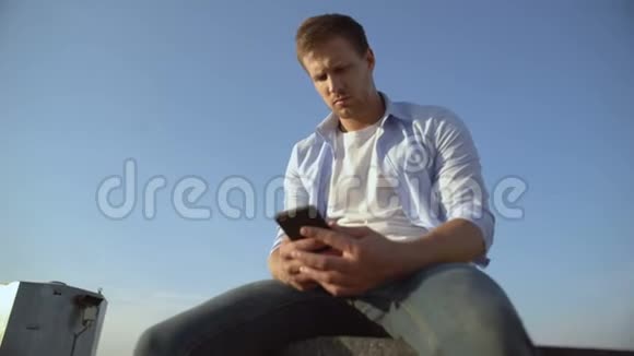 女朋友分手后沮丧的男性智能手机坐在屋顶边缘视频的预览图